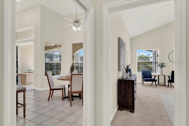 hallway featuring light colored carpet, baseboards, high vaulted ceiling, and light tile patterned flooring