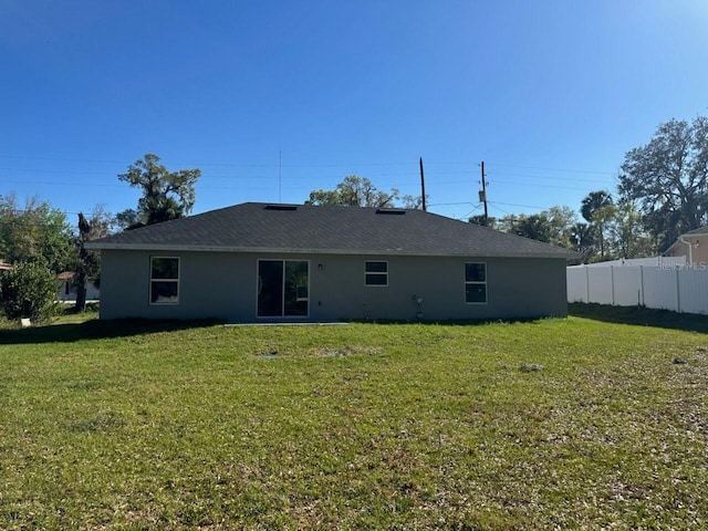 rear view of property with stucco siding, a lawn, and fence