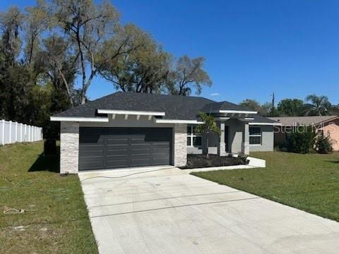 view of front of home featuring an attached garage, a front lawn, fence, stone siding, and driveway