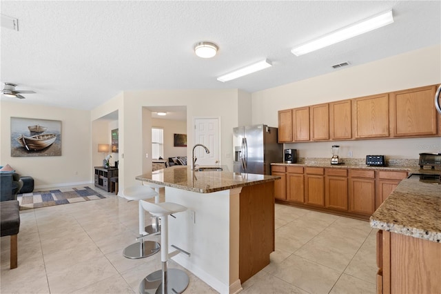 kitchen with visible vents, light stone countertops, a breakfast bar area, stainless steel fridge, and a sink