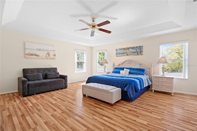 bedroom featuring a tray ceiling, baseboards, light wood finished floors, and a textured ceiling