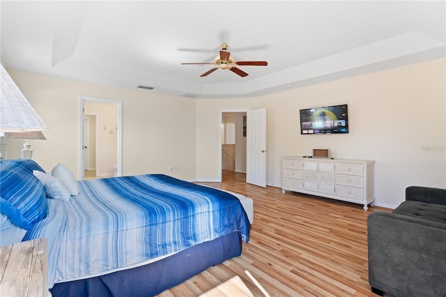 bedroom with visible vents, ceiling fan, baseboards, a tray ceiling, and light wood-style floors