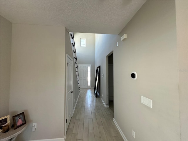 corridor with light wood finished floors, a textured ceiling, and baseboards