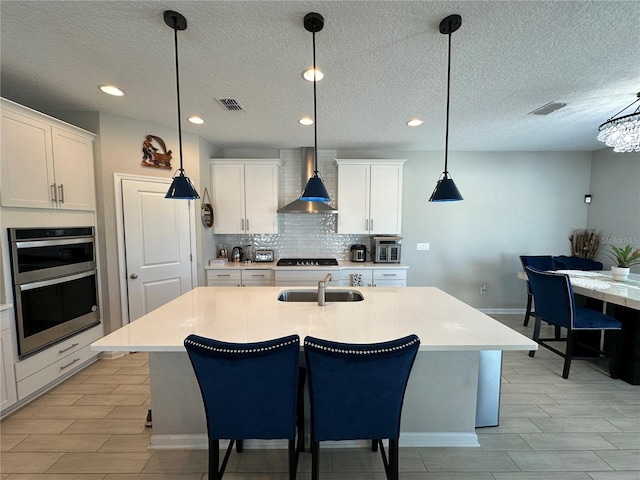 kitchen featuring visible vents, stainless steel double oven, gas stovetop, wall chimney exhaust hood, and a sink