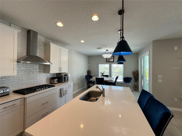 kitchen with tasteful backsplash, wall chimney range hood, stainless steel gas cooktop, light countertops, and a sink