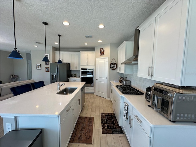 kitchen with wood finish floors, visible vents, a sink, appliances with stainless steel finishes, and wall chimney exhaust hood