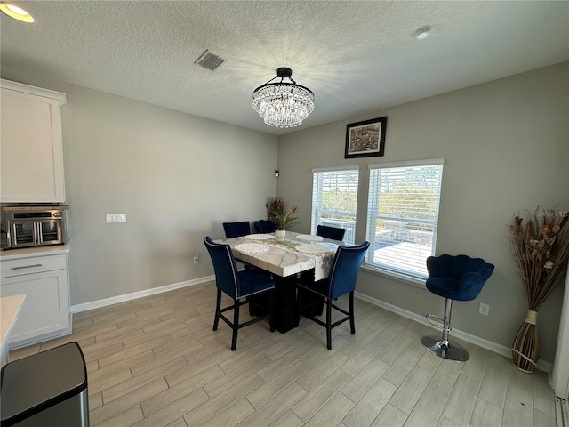 dining room featuring visible vents, a textured ceiling, an inviting chandelier, light wood finished floors, and baseboards