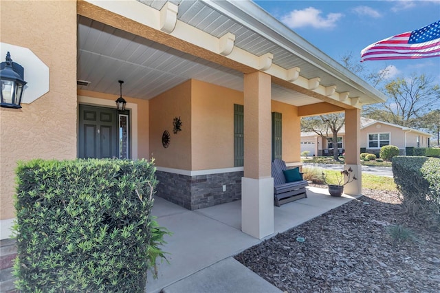 view of exterior entry with stucco siding, stone siding, and a porch