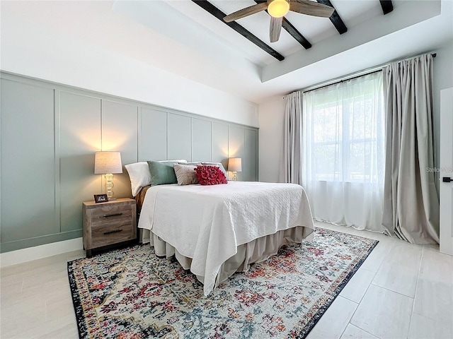 bedroom featuring a decorative wall, beamed ceiling, and ceiling fan