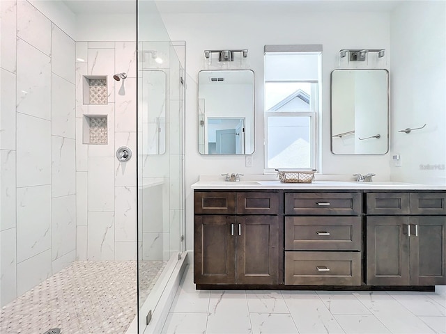 bathroom featuring double vanity, marble finish floor, a tile shower, and a sink