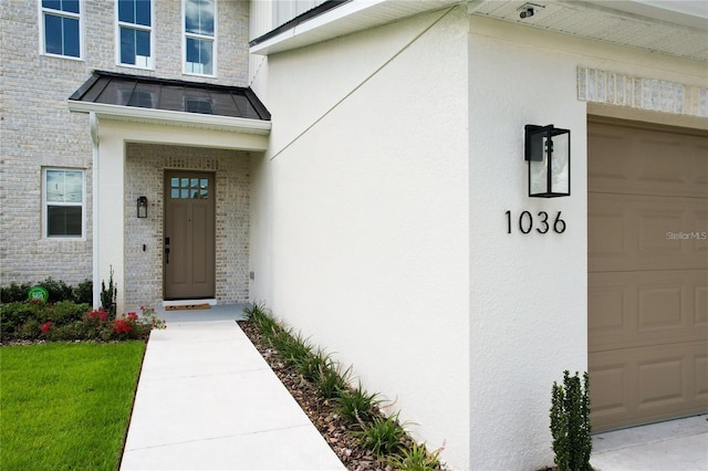 view of exterior entry featuring brick siding, stucco siding, metal roof, an attached garage, and a standing seam roof