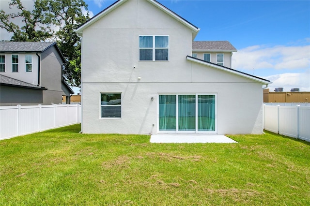 rear view of property with stucco siding, a lawn, and a fenced backyard