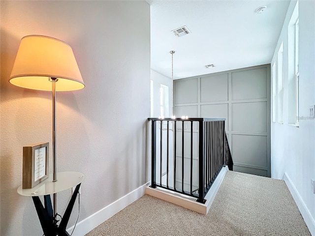 hallway featuring visible vents, baseboards, carpet flooring, and a decorative wall