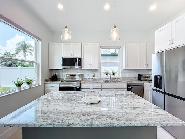 kitchen with backsplash, pendant lighting, appliances with stainless steel finishes, white cabinets, and a sink