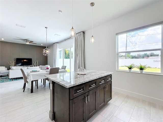 kitchen featuring open floor plan, hanging light fixtures, baseboards, dark brown cabinets, and light stone countertops