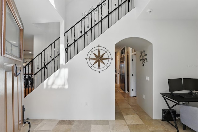 staircase with arched walkways, a towering ceiling, and stone tile flooring