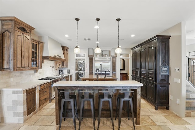 kitchen featuring a center island with sink, light countertops, custom range hood, premium appliances, and stacked washer / drying machine