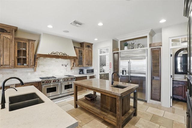 kitchen featuring custom exhaust hood, high quality appliances, tasteful backsplash, and a sink