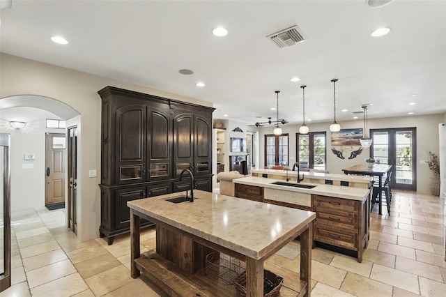 kitchen featuring visible vents, a large island with sink, recessed lighting, arched walkways, and a sink