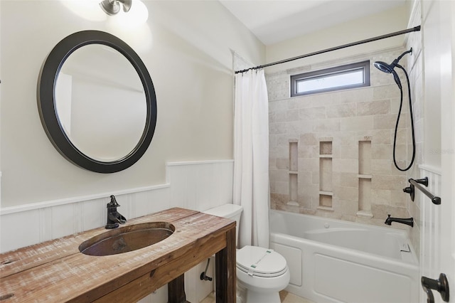 bathroom with toilet, shower / bathtub combination with curtain, a wainscoted wall, and a sink