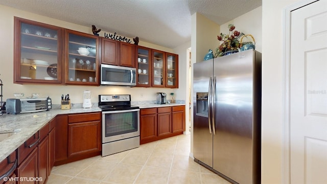 kitchen featuring light stone counters, light tile patterned floors, glass insert cabinets, appliances with stainless steel finishes, and a textured ceiling