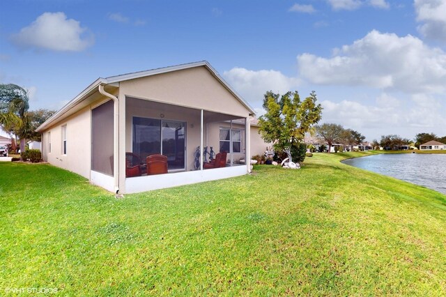 rear view of property with stucco siding, a sunroom, a yard, and a water view