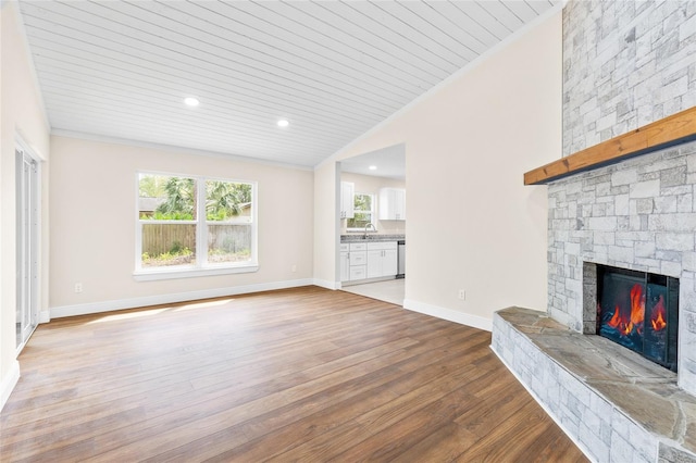 unfurnished living room with baseboards, vaulted ceiling, ornamental molding, a fireplace, and wood finished floors