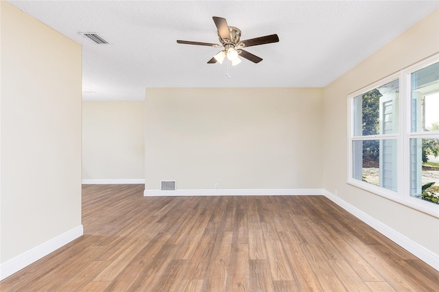 spare room featuring a ceiling fan, visible vents, wood finished floors, and baseboards