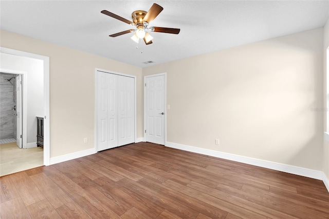 unfurnished bedroom with visible vents, ensuite bath, wood finished floors, a closet, and baseboards