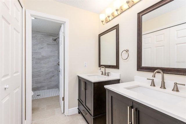 full bathroom with a sink, tiled shower, and two vanities