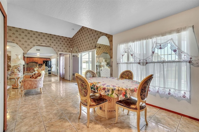 dining space with baseboards, wallpapered walls, lofted ceiling, light tile patterned flooring, and a textured ceiling