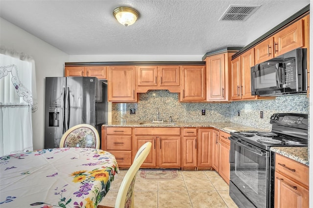 kitchen featuring visible vents, black appliances, a sink, tasteful backsplash, and light stone countertops