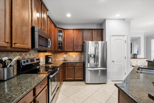 kitchen featuring dark stone counters, light tile patterned floors, decorative backsplash, stainless steel appliances, and a sink