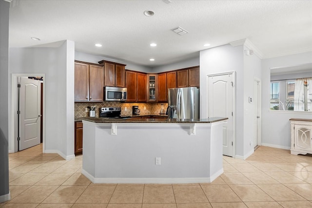 kitchen featuring visible vents, light tile patterned flooring, decorative backsplash, appliances with stainless steel finishes, and a kitchen breakfast bar