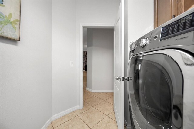 washroom featuring light tile patterned floors, baseboards, washer / clothes dryer, and cabinet space