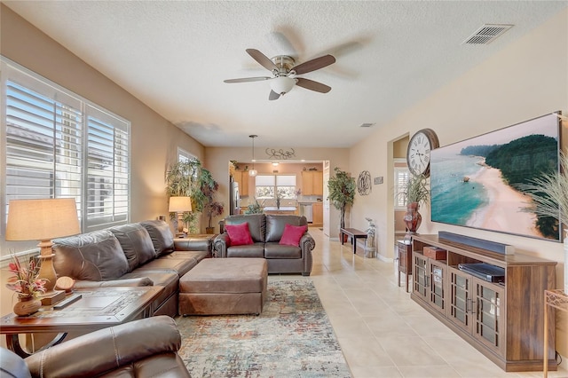 living area featuring light tile patterned floors, visible vents, a textured ceiling, and a ceiling fan