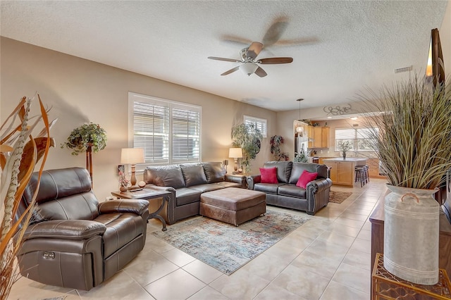 living area featuring light tile patterned flooring, a ceiling fan, visible vents, and a textured ceiling