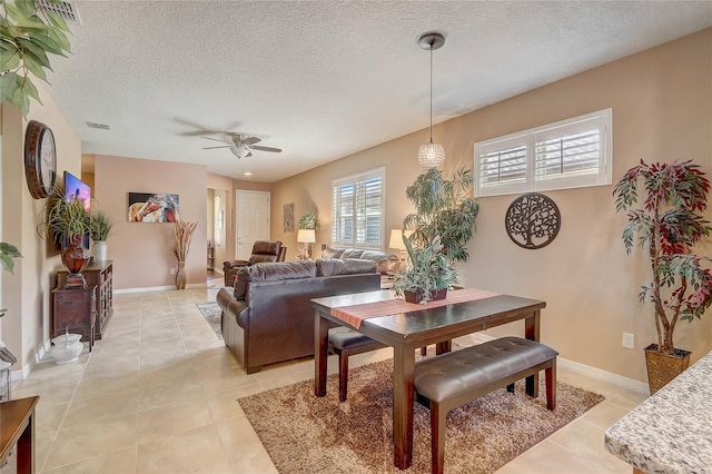 dining room with a ceiling fan, visible vents, baseboards, light tile patterned flooring, and a textured ceiling