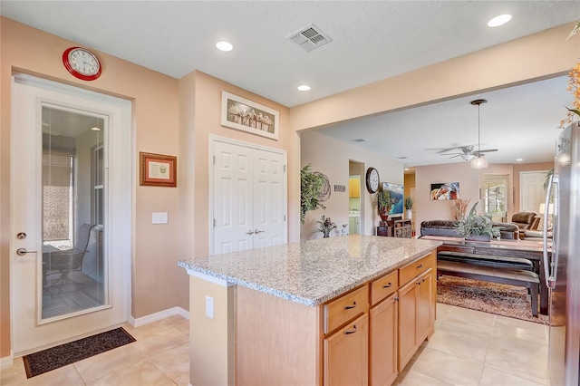 kitchen featuring visible vents, open floor plan, a center island, freestanding refrigerator, and light stone countertops