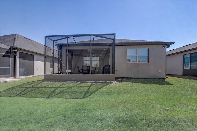 back of house featuring a yard, ceiling fan, glass enclosure, and stucco siding