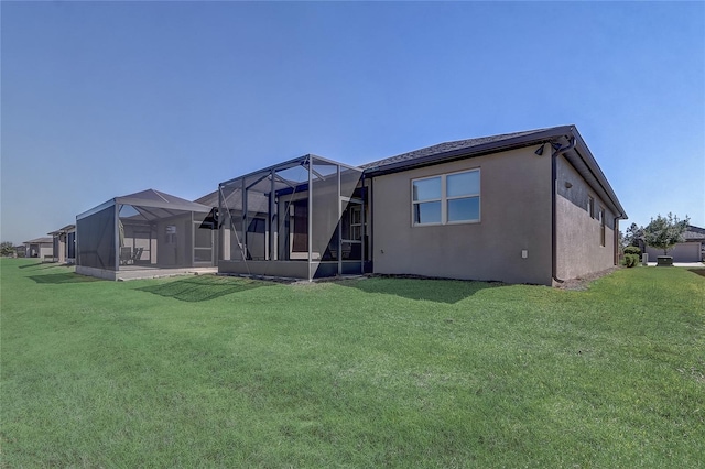 rear view of house featuring stucco siding, a lawn, and glass enclosure