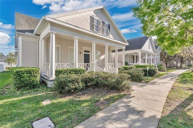 view of front of home featuring a shingled roof, a front yard, covered porch, and stucco siding