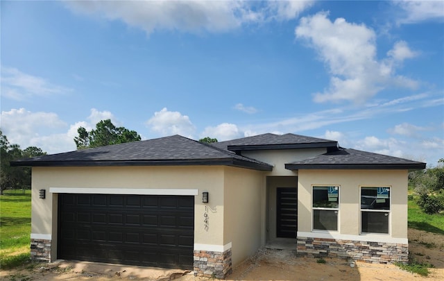 prairie-style home with stucco siding, stone siding, and an attached garage