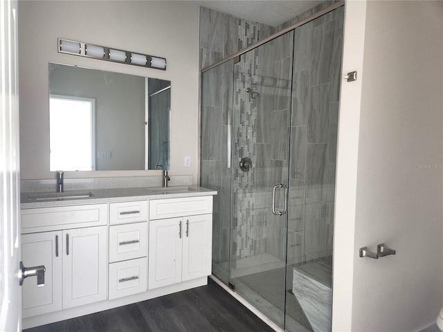 bathroom with double vanity, a stall shower, wood finished floors, and a sink