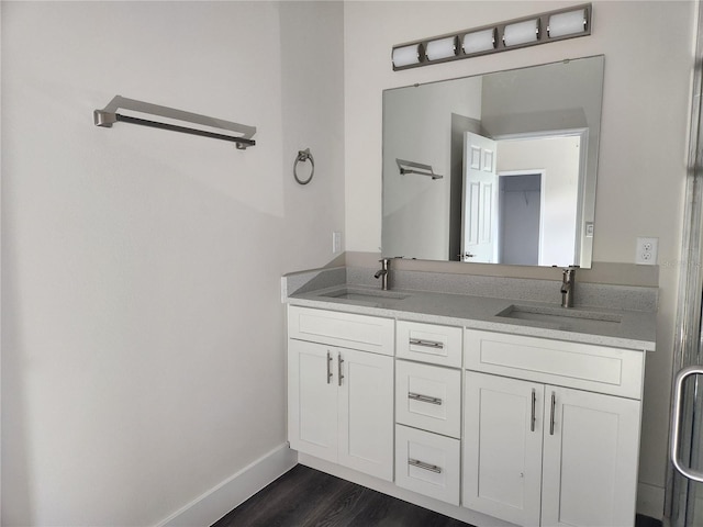 full bath with double vanity, wood finished floors, baseboards, and a sink