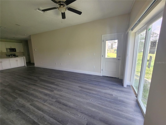 unfurnished living room featuring visible vents, baseboards, dark wood-style floors, and a ceiling fan