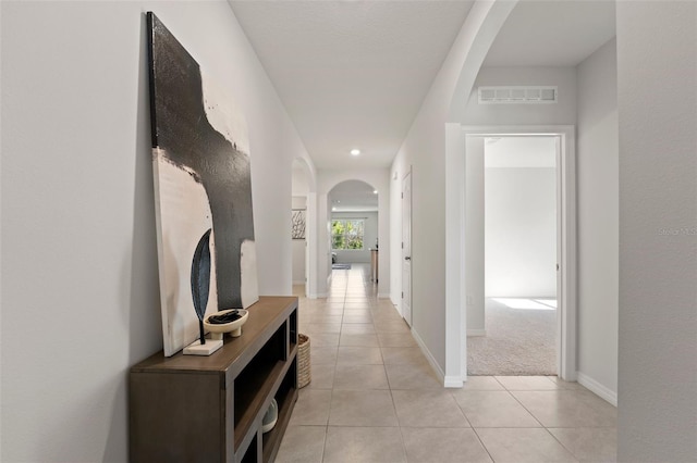 hall with light tile patterned floors, visible vents, baseboards, and arched walkways