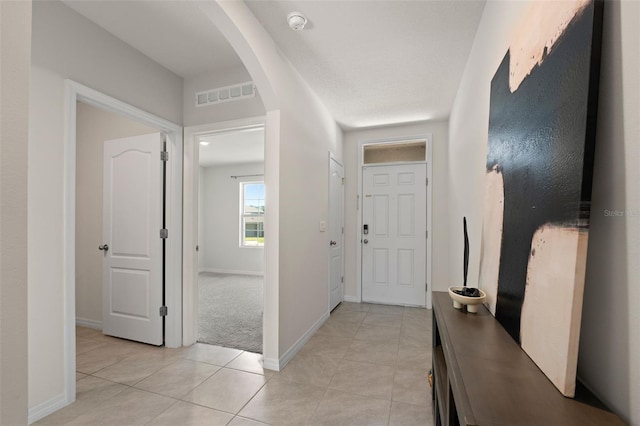 corridor with arched walkways, visible vents, baseboards, and light tile patterned floors