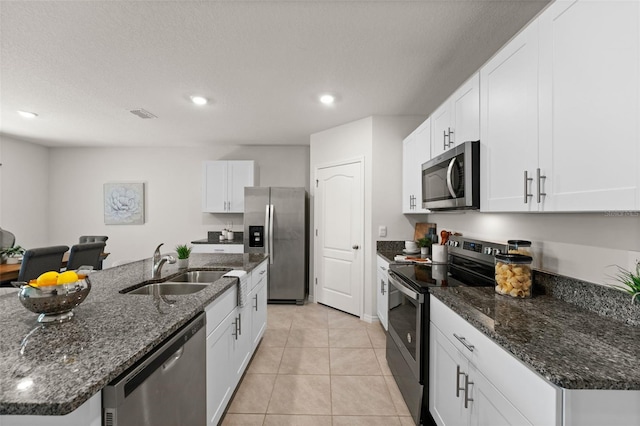 kitchen with an island with sink, appliances with stainless steel finishes, light tile patterned flooring, white cabinets, and a sink