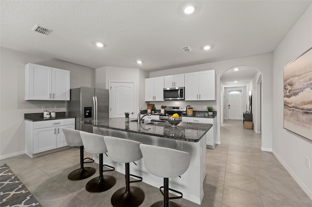 kitchen with visible vents, a breakfast bar, a sink, arched walkways, and appliances with stainless steel finishes